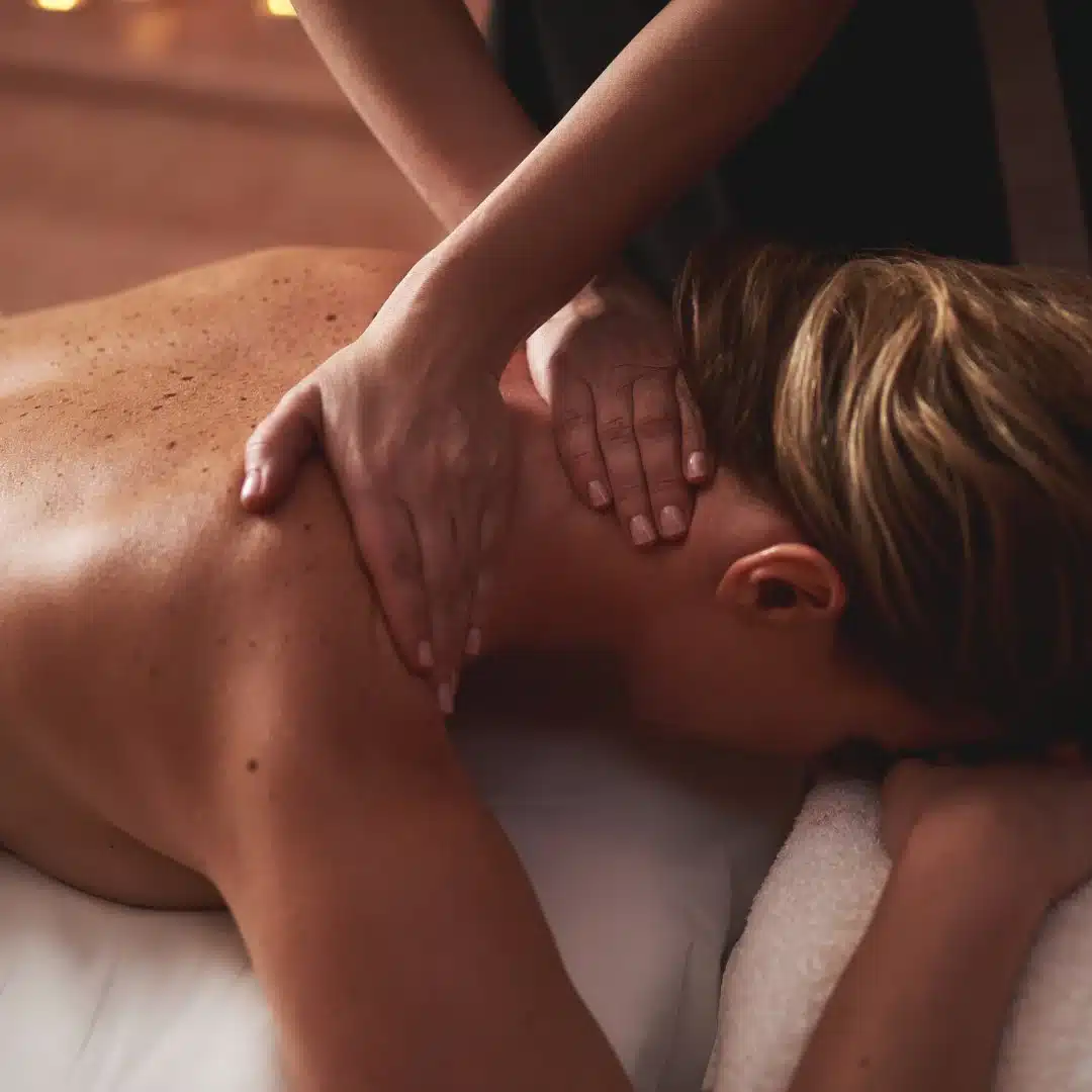 A person receives a relaxing massage on their shoulders and upper back while lying face down on a massage table, with soft lighting creating a calm atmosphere.