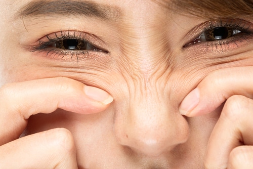 A close-up of a person pinching the skin on their nose, causing wrinkles to form around their eyes and nose. The person’s eyes are partially closed, and their eyebrows are slightly raised.