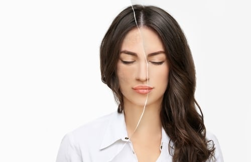 A person wearing gloves holds a test tube filled with yellow liquid, next to a laboratory centrifuge with its lid open. The centrifuge has a digital control panel and several other test tubes placed inside.