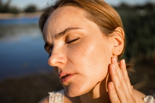 A close-up of a person undergoing laser treatment on their shoulder. A professional wearing blue gloves operates a handheld laser device, shown emitting a green light onto the skin. The scene is clinical and focused on medical procedures.