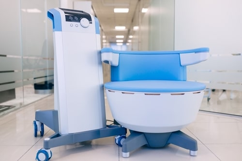 A close-up of a person holding a magnifying glass over a mole on another persons bare back, examining it for medical analysis. The setting appears to be a clinical environment.
